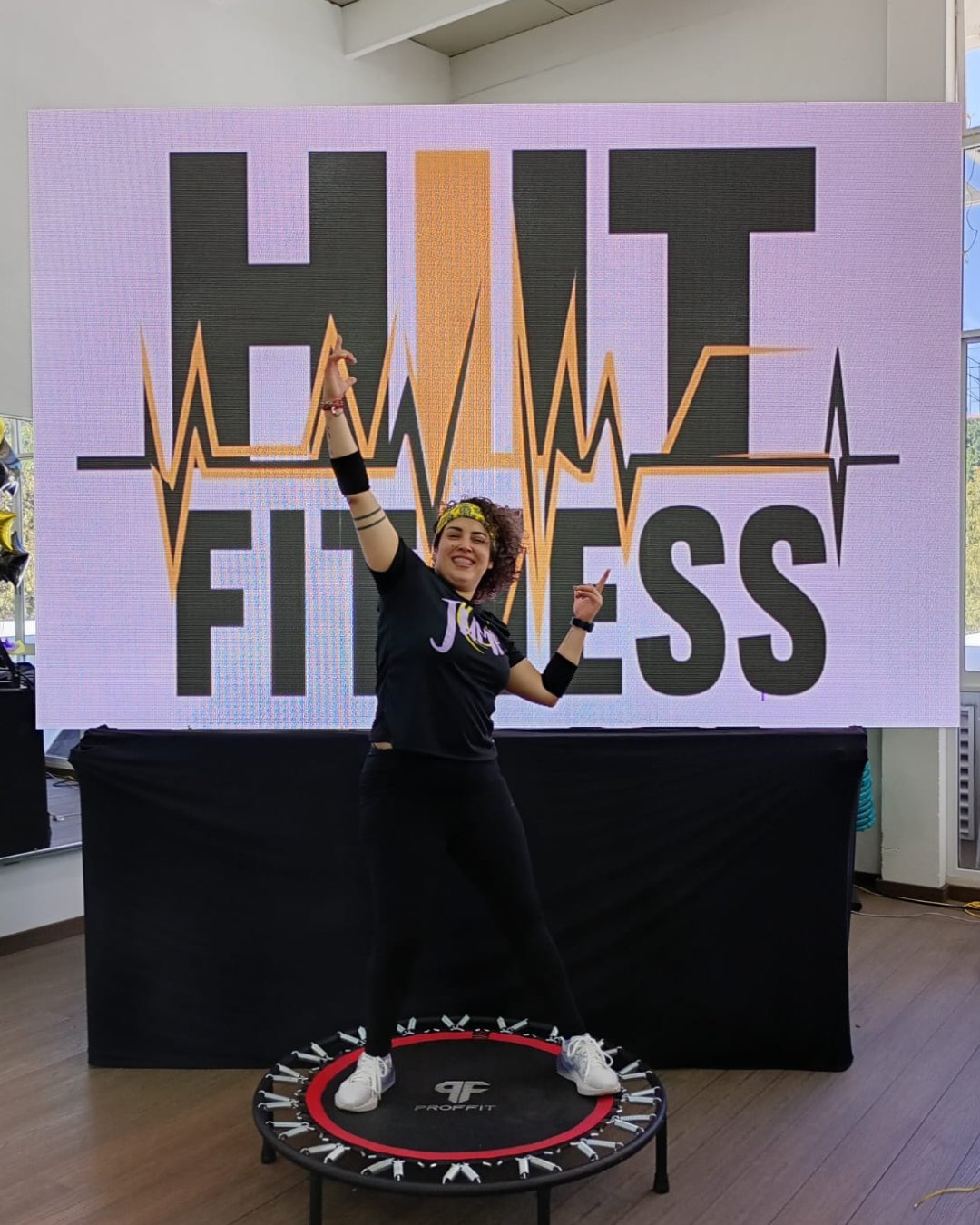 Coach Berenice Bravo en clase frente al logo HIIT FITNESS
